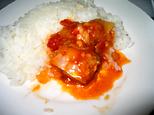 ライスの横に鶏肉の料理を乗っけて、ご飯と一緒に食べている様子。ソースの赤っぽい色がスパイシーさを物語っています