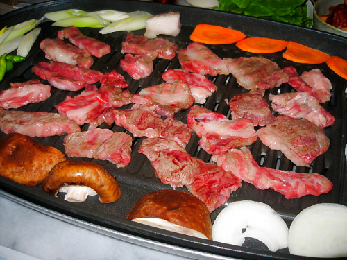 お肉用の網目のホットプレートに、半分焼色がついてきたお肉、周りに人参、しいたけ、玉葱、白ねぎ、ししとうが。