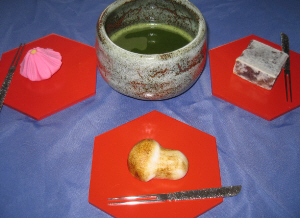 ブルーのクロスに、赤い木製の銘々皿が3つ、その上に和菓子が乗せられて、真ん中に抹茶茶碗が置いてあります。