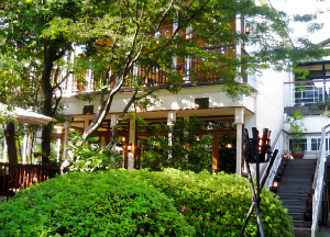 植木と木立の向こうに、大きな窓の建物が見えています。庭には背の高さくらいの位置にかがり火が燃えていて、雰囲気をかもし出しています。