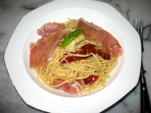 真ん中が窪んでいる白い八角形のお皿。パスタとドライトマトの赤、生ハムのピンク、トッピングに飾ったスイートバジルの緑が色鮮やかな一皿です。