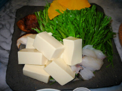 グレーの四角い大きめの平皿に、豆腐や野菜タラなどが盛り付けられています。黄色く見えているのは銀杏の葉のようです。