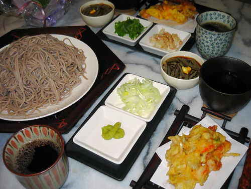 小さめの竹細工の上に乗った天ぷら、やはり大きめの竹細工の上にお皿、その上にお蕎麦が。どちらもこげ茶色に塗られた竹細工。つけ汁が入っているのは黒っぽい器、薬味は白い小角皿にそれぞれ乗せられています。丸い白い小さな器にじゅんさい、そして湯飲み茶碗には何か飲み物が入っています。