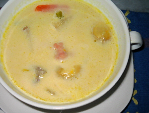 スープのアップ画像。白いカップソーサーと白いカップスープ。スープの優しい黄色実が食欲をそそります。