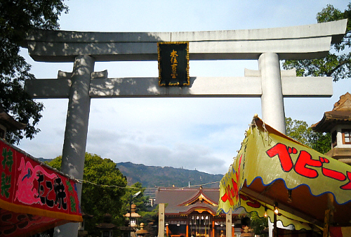 神社入り口の鳥居。入り口の前に2軒だけ出店がでていました。ベビーカステラとたこ焼きの垂れ幕が見えています。