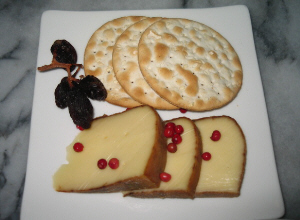 四角い白い平皿、クラッカーとチーズがそれぞれ3つずつ。干しブドウとピンクペッパーが彩りに添えられています。