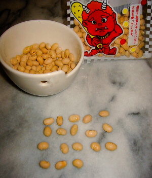 テーブルの上に白い小さな器の中に豆が入っています。豆の袋もすぐそばにあって、その袋には赤鬼のイラストが書いてあります。器の手前に前が並べられていて、数えると全部で18個あります。