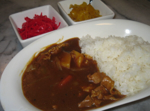 白いカレー皿に盛られたカレーライス。薬味は四角い白い器に、紅しょうがと、沢庵がそれぞれ盛られています。