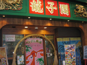 龍子閣と書かれたお店の入り口。写真入の大きなメニュー看板が入り口に置かれています。緑色の屋根に真っ赤なパネル、そこのお店の名前が金文字で書かれてあります。