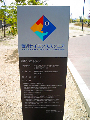 灘浜サイエンススクエアの入り口の看板。縦長の四角い看板で、7対3の7の下の部分は黒、3の部分がグレーで、サイエンススクエアのマークと名前がブルーで画かれてあります。黒い部分には館内利用案内が書かれてあります。