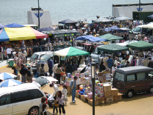 海がすぐ側のフリーマーケット会場。車やカラフルなテント、積み上げられたダンボール、行きかう人々、かなり賑わっている会場です。