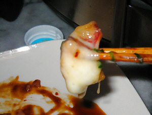 焼きあがったタコを橋で摘み上げている写真。とろっとチーズが全体に絡んでいます。