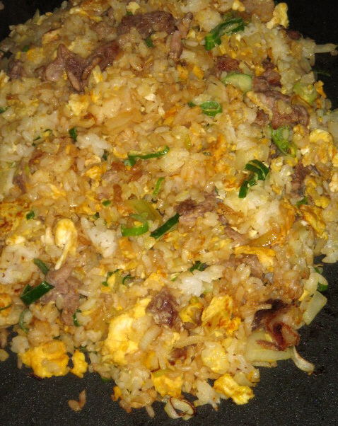 ホットプレートの上で調理された焼き飯のアップ画像。卵やネギなどの具材とご飯が混ざり合って美味しそうです。