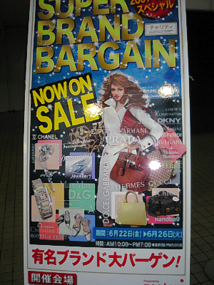 バーゲン会場に飾られていたバーゲンの看板。有名ブランド大バーゲンと書かれてあり、女性がたくさんのバックを腕にぶら下げているイラストが描かれています。