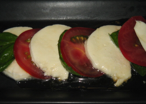 黒い長方形のお皿に、モッツァレラの白、トマトの赤、バジルの緑、それらが交互に並べられ色鮮やかなお皿になっています。