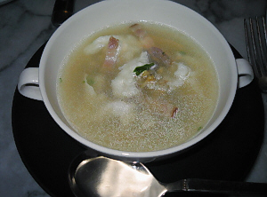 黒い丸皿の上に白い両手持ちのスープカップが。ベーコンと白っぽいものがスープから顔を覗かせています。