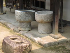 石の臼のようなもが二つ並んでいます。手前には何かの器具の土台だった穴が二つ開いた四角い石も見えます。